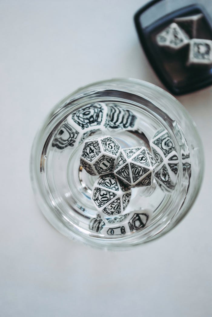 A close-up of intricately designed dice inside a glass cup viewed from above on a white background.